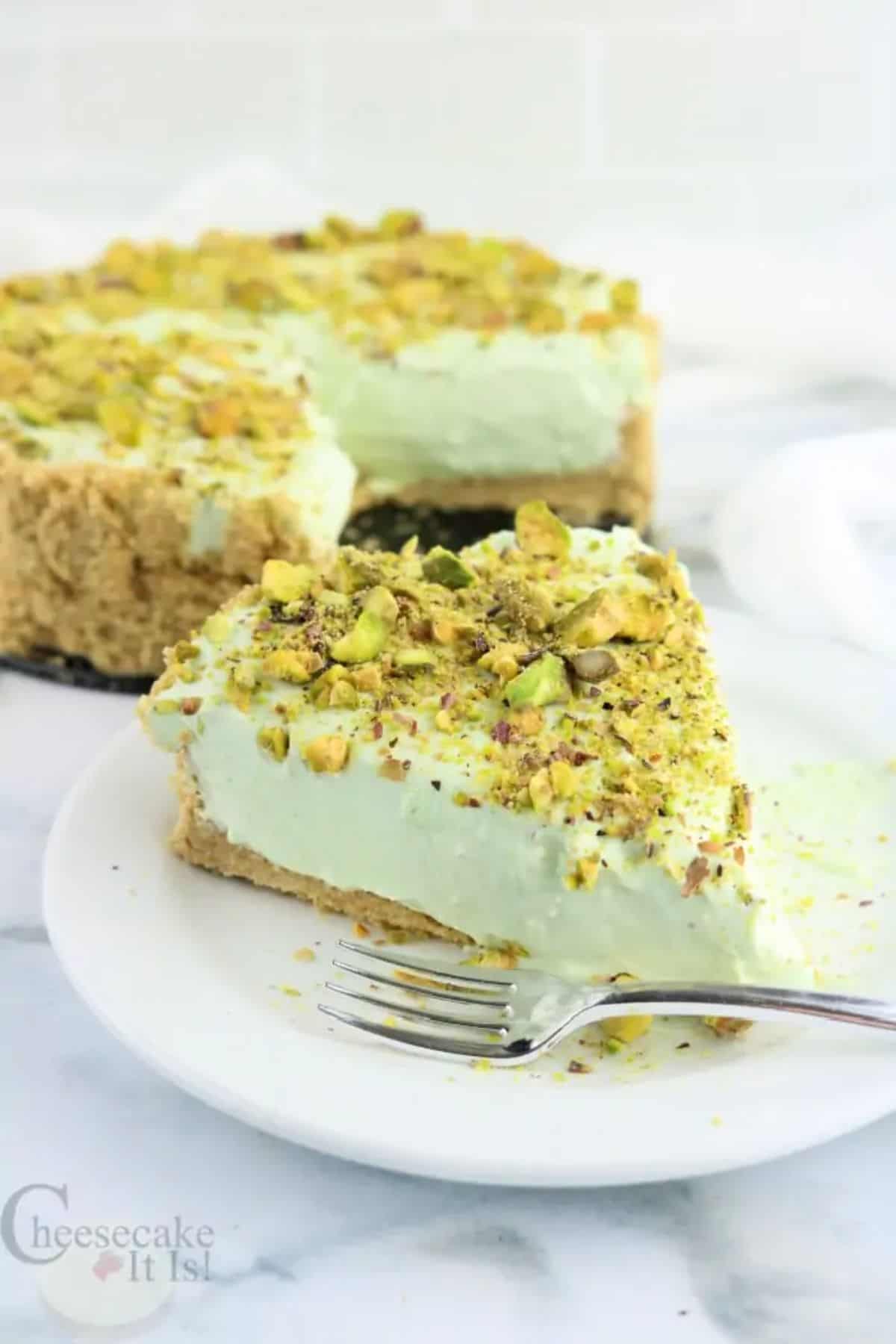 A piece of No-Bake Pistachio Cheesecake on a white plate with a fork.