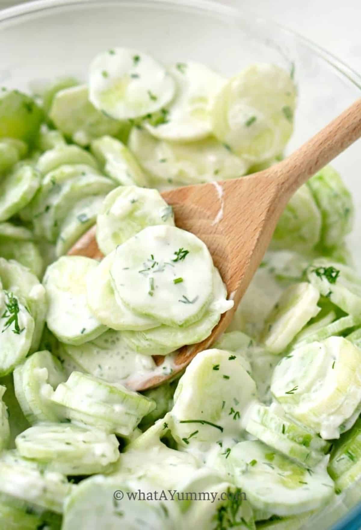 Cucumber Dill Salad in a glass bowl with a wooden spatula.