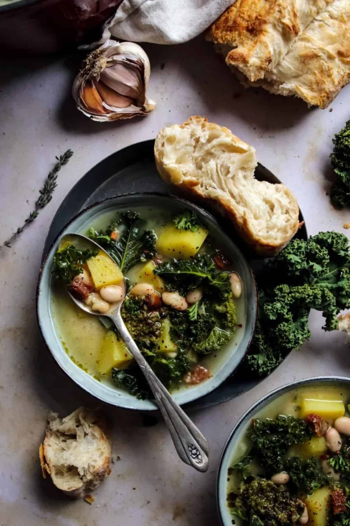 Vegan Zuppa Toscana on a blue plate with a spoon and a piece of bread.