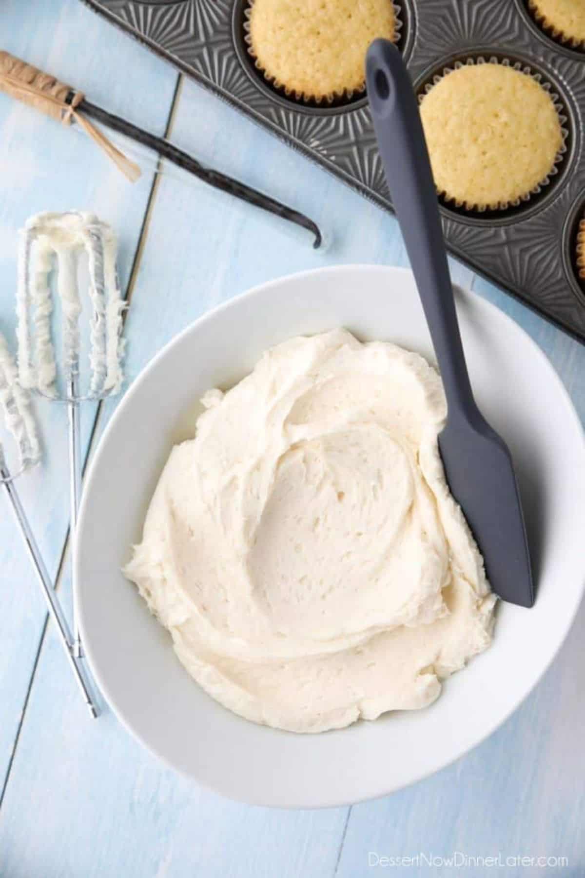 Vanilla Buttercream Frosting in a white bowl with a black spatula.