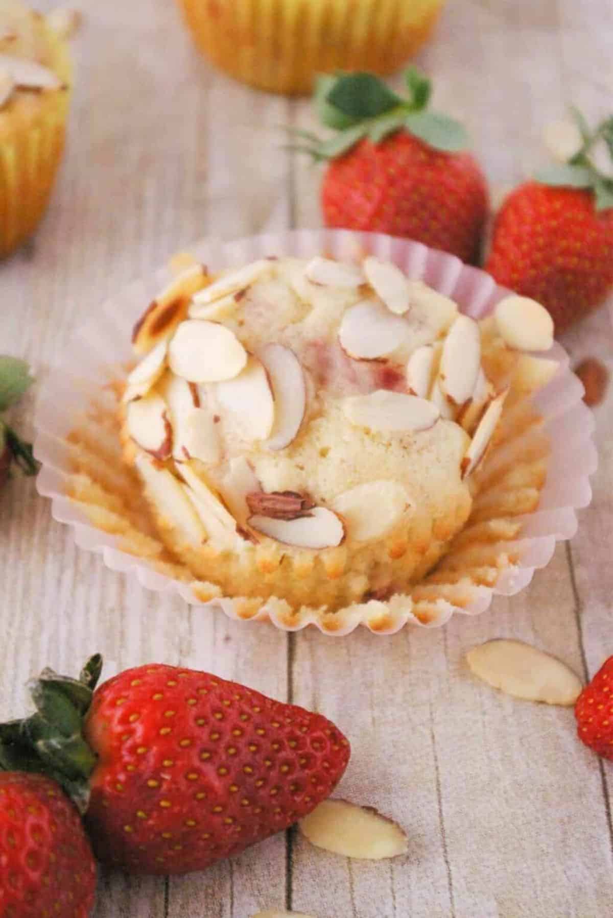 Strawberry Muffin with Almonds with scattered strawberries on a wooden table.