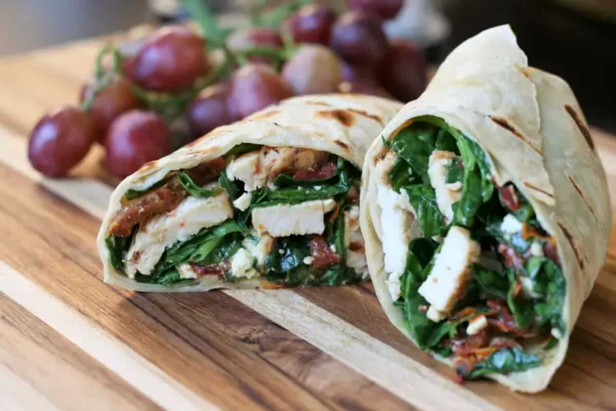 Chicken, Feta, and Sun-dried Tomato Wraps with grapes on a wooden tray.