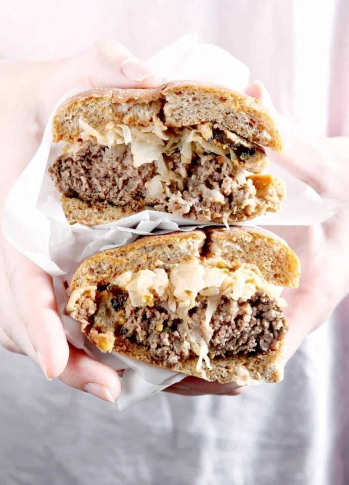 Scrumptious Sauerkraut Burgers with Oven Fried Pickles held by hands.