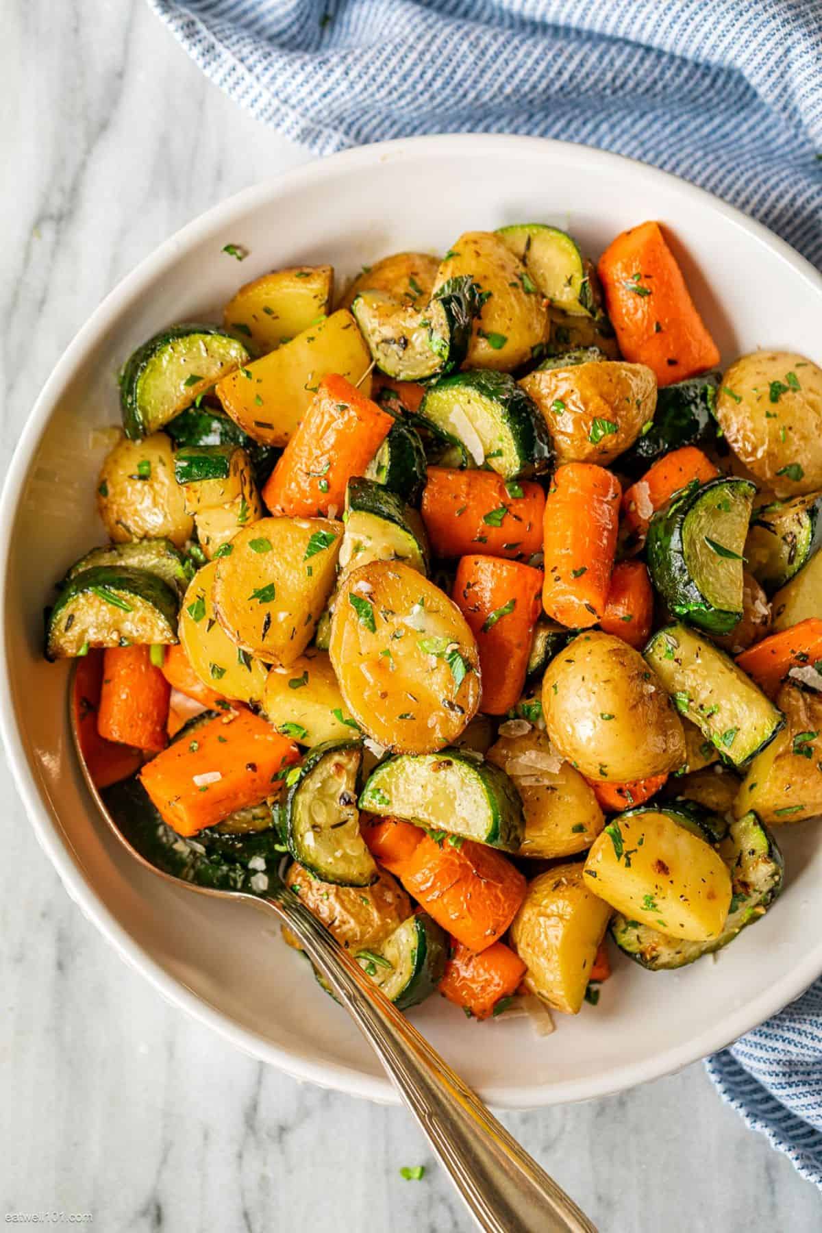 Delicious Garlic Herb Roasted Potatoes, Carrots, and Zucchini in a white bowl with a spoon.