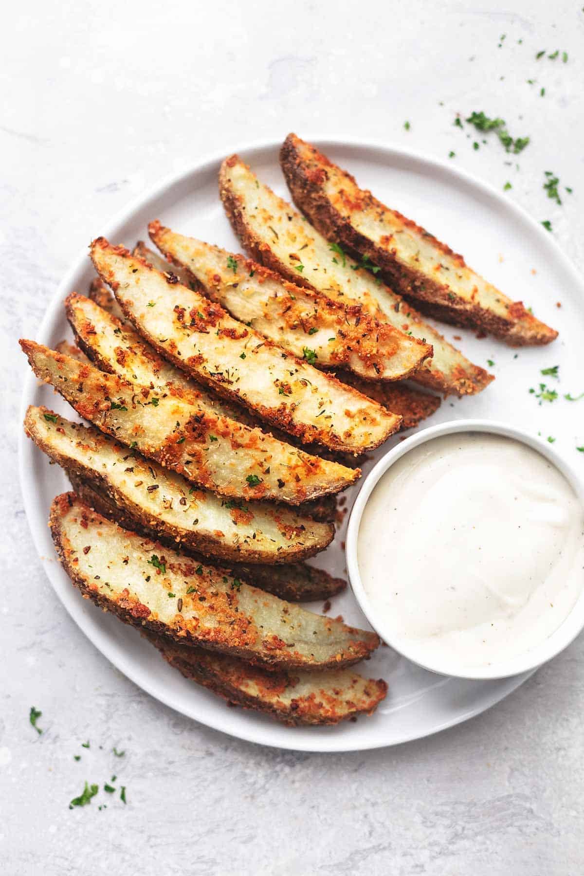 Delicious Baked Garlic Parmesan Potato Wedges with a bowl of dip on a white tray.