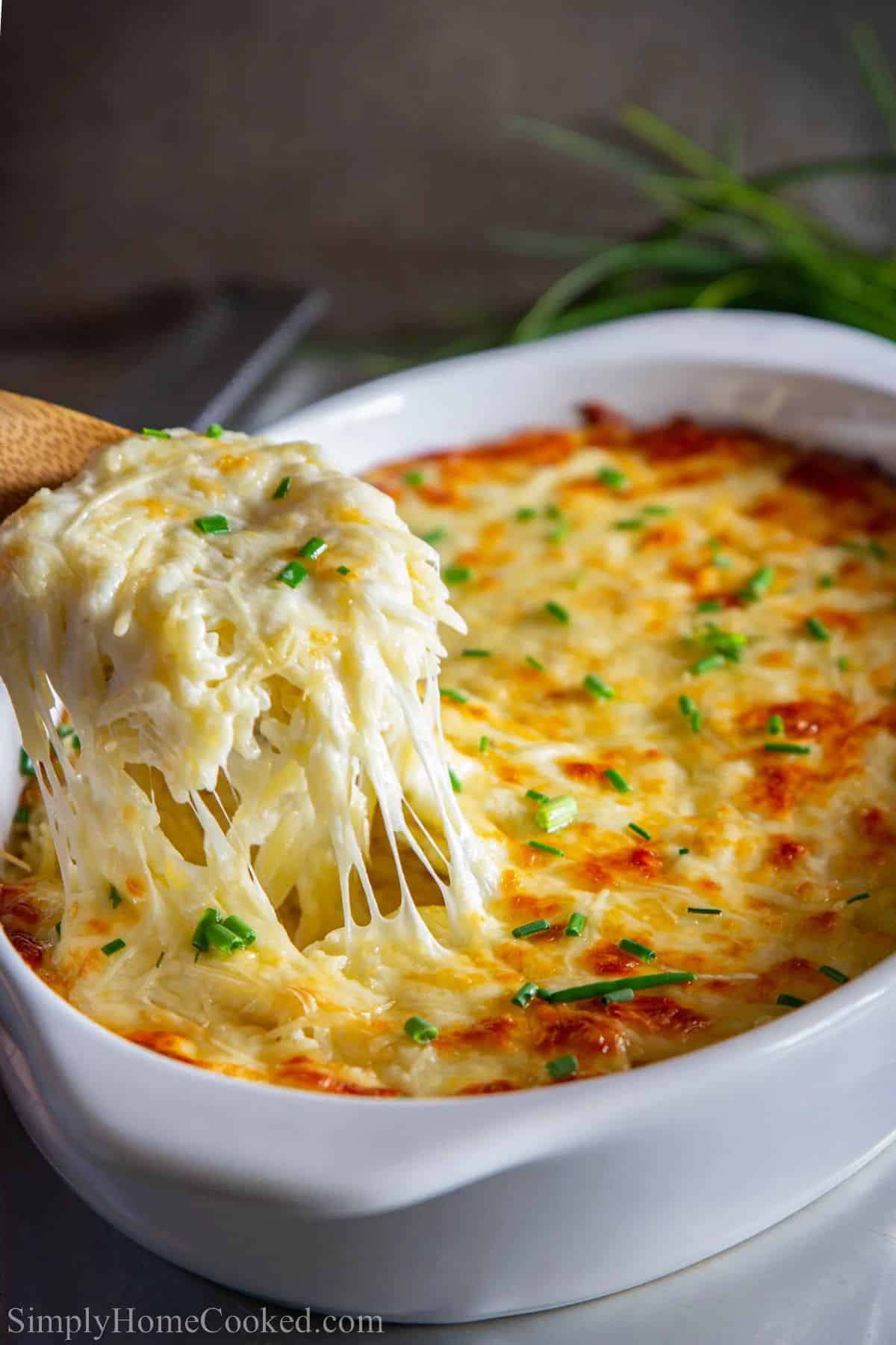 Delicious Creamy Orzo in a white casserole picked by a wooden spatula.