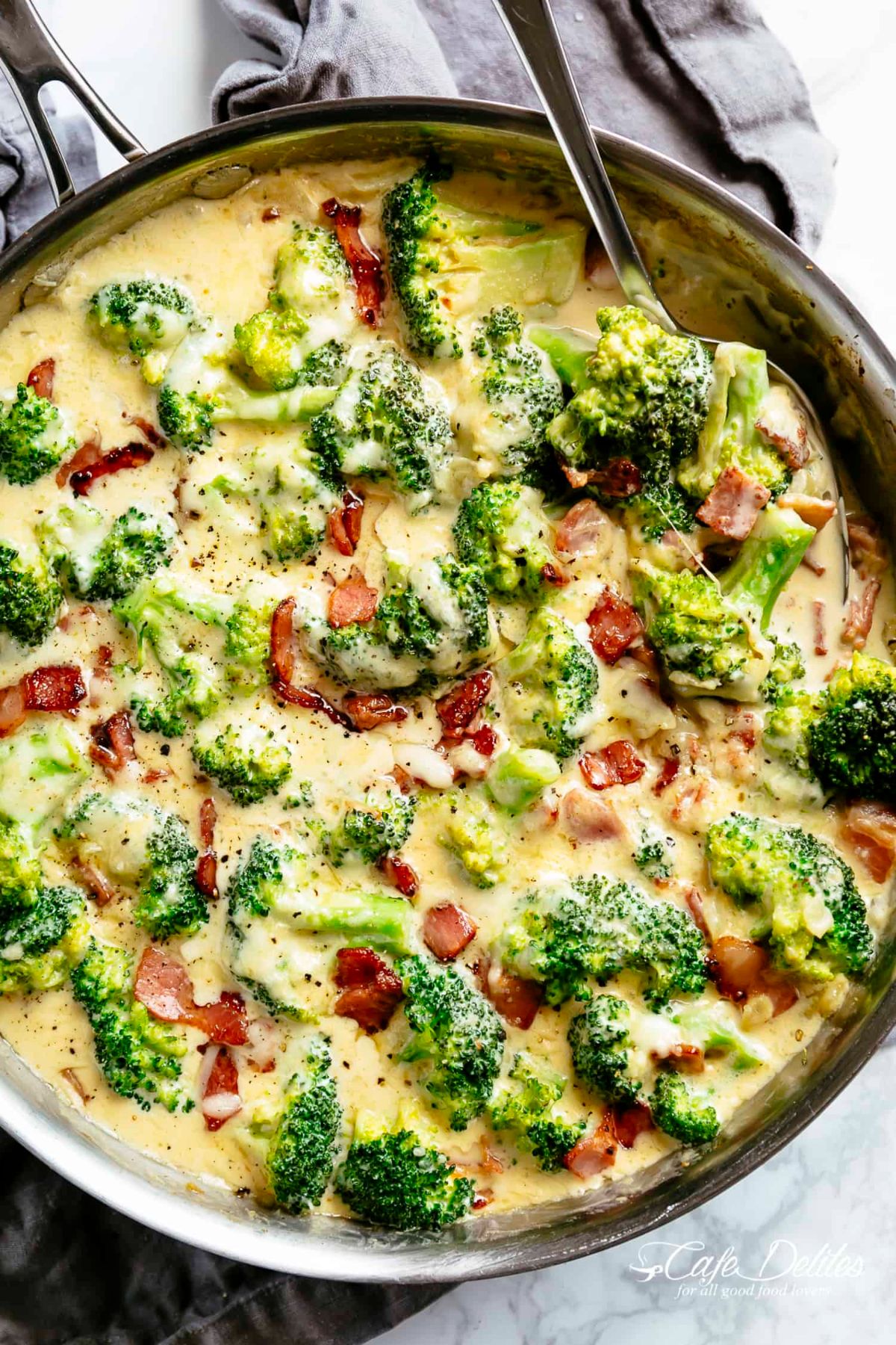 Creamy Garlic Parmesan Broccoli With Bacon in a skillet with a spoon.